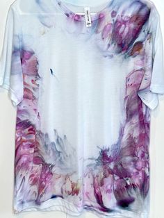 a white t - shirt with pink and purple flowers on the front, hanging from a clothes line