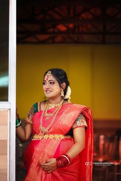 a woman in a red and gold sari is looking out the window with her hand on her hip