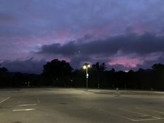 an empty parking lot at night with street lights and dark clouds in the sky above