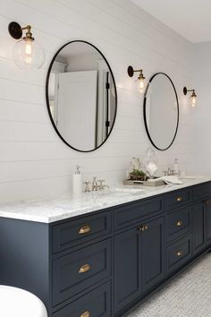 two sinks and mirrors in a bathroom with white tile flooring, blue cabinets and gold pulls