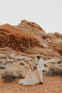 a bride and groom standing in the desert with red rock formations behind them at their wedding