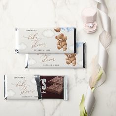 two chocolate bars with teddy bears on them sitting next to some flowers and feathers in the background