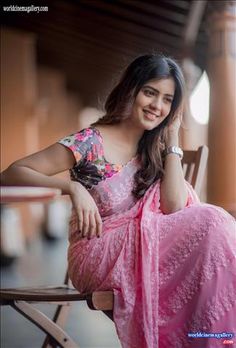 a woman in a pink sari sitting on a wooden chair smiling at the camera