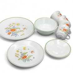 four plates and two cups with flowers painted on them, sitting next to each other