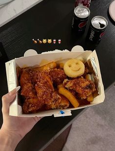 a person holding up a box of chicken wings and pretzels with two sodas in the background