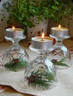 three clear glass candlesticks sitting on top of a white table cloth next to a potted plant