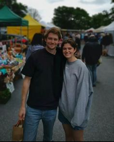 a man and woman standing next to each other in front of tents with umbrellas