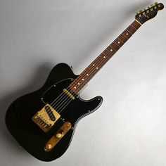 an electric guitar is sitting on a white surface and it's black with gold hardware