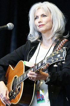 a woman with grey hair playing an acoustic guitar at a music festival in front of a microphone