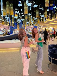 two young women standing next to each other in front of a large chandelier