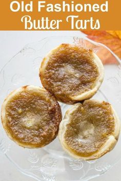 three old fashioned butter tarts sitting on top of a glass plate with leaves in the background