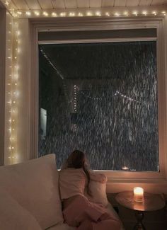 a woman sitting on a couch in front of a window covered in snow and lights