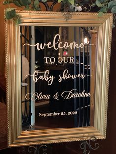 a mirror with the words welcome to our baby shower written on it and greenery