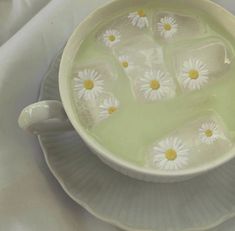 a bowl filled with water and daisies sitting on top of a white table cloth