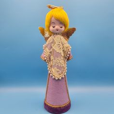 a doll with yellow hair and wings is standing on a blue background wearing a purple dress