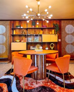 a dining room with orange chairs and a round table surrounded by shelves filled with plants