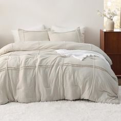 a bed with white sheets and pillows in a room next to a dresser, mirror and lamp