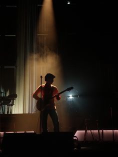 a man standing on top of a stage with a guitar in his hand and lights behind him