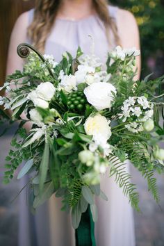 a woman holding a bouquet of flowers in her hands and wearing a white dress with green accents