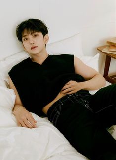 a young man laying on top of a bed next to a white comforter and pillows