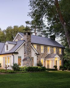 a white house with stone and shingles on the roof, surrounded by green grass