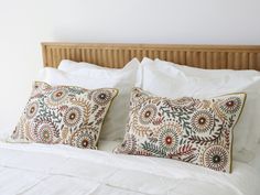 two pillows on top of a bed with white linens and wood headboard in the background