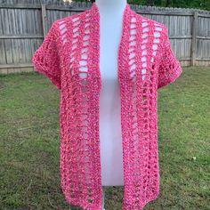 a pink crocheted cardigan on a mannequin in front of a fence