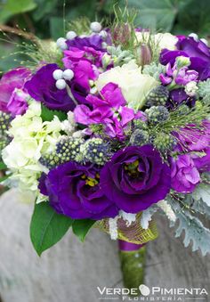 a purple and white bouquet with greenery in the middle is sitting on a bench