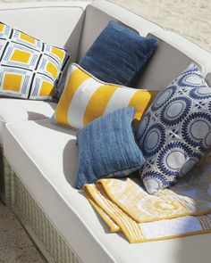 a white couch with yellow and blue pillows on it's back end, next to the beach