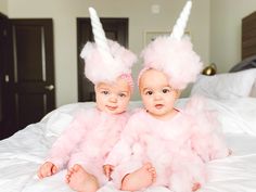 two babies wearing bunny ears and pink fluffy outfits on a bed with white linens