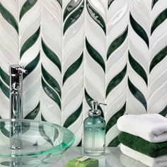 a bathroom with green and white tiles on the wall, glass sink and soap dispenser