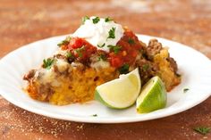 a slice of mexican casserole on a plate with sour cream and lime wedges