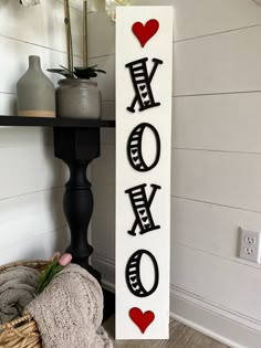 a wooden sign with the word love spelled in black and red on it next to a basket of flowers