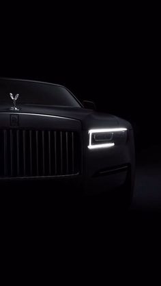 the front end of a black rolls royce in the dark with its headlights turned on