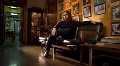 a man sitting on top of a black chair in a room filled with framed pictures