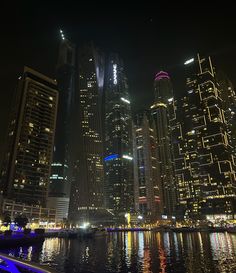 the city skyline is lit up at night and reflecting in the water with bright lights