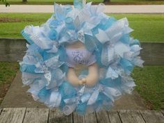 a blue and white wreath with a teddy bear in the center on a wooden deck