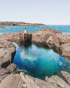 a person sitting on some rocks by the ocean with blue water in front of them