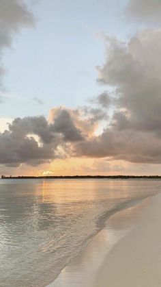 the sun is setting over the water at the beach with white sand and blue sky