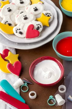 decorated cookies and icing sitting on top of a table next to bowls of food