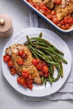 a white plate topped with chicken, green beans and tomatoes next to a casserole dish