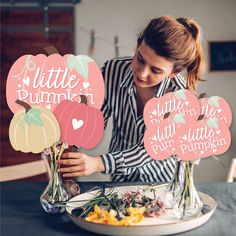 a woman sitting at a table with flowers in vases and paper cutouts that say little pumpkin