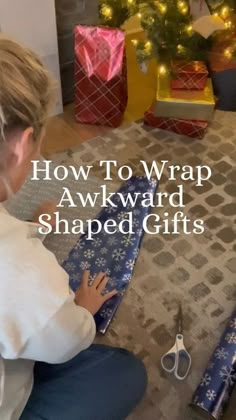 a woman sitting on the floor next to a christmas tree and wrapping her presents with scissors