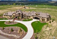 an aerial view of a large home in the middle of a grassy field with mountains in the background