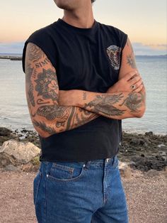 a man with tattoos standing in front of the ocean