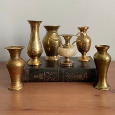 an assortment of brass vases sitting on top of a wooden table next to a book