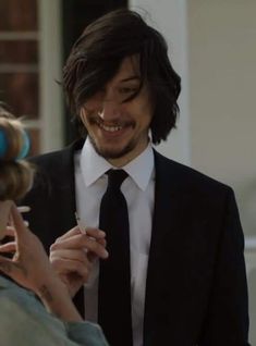 a man in a suit and tie smiles as he fixes his tie on another woman's head