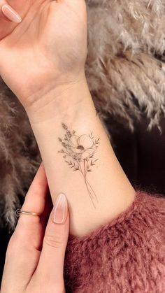 a woman's wrist with a small flower tattoo on the left side of her arm