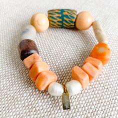 Sustainable Bracelet. A bright bold green hand painted prayer bead with neutral rosewood and soft peach beads. African prayer beads from Africa’s Ivory Coast for loyalty, love and health. Featuires orange coral stone. Rosewood from the tree of health and wisdom. Freshwater large pearls in mint. Sterling silver BelleStyle logo tag. Comes in linen travel pouch. One of a kind. Made in USA. Artisan Wooden Beads Bracelet For Meditation, Artisan Wooden Beads Bracelets For Meditation, Earthy Wooden Beaded Bracelets As Gift, Earthy Wooden Beaded Bracelets For Gift, Artisan Orange Hand-strung Beaded Bracelets, Spiritual Wooden Beads Stretch Bracelet For Healing, Handmade Orange Beaded Bracelets For Meditation, Unique Wooden Beads Bracelet For Healing, Handmade Spiritual Orange Stretch Bracelet