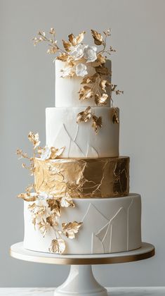 a three tiered cake with gold leaf decorations on the top and bottom, sitting on a white pedestal